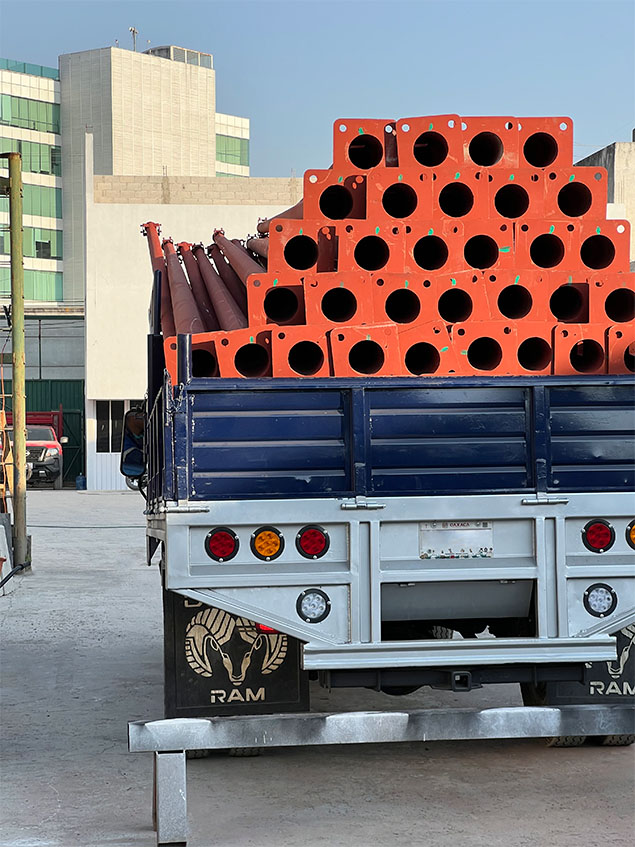 Camión cargado con postes metálicos con primario rojo óxido y placa base, listos para entrega
