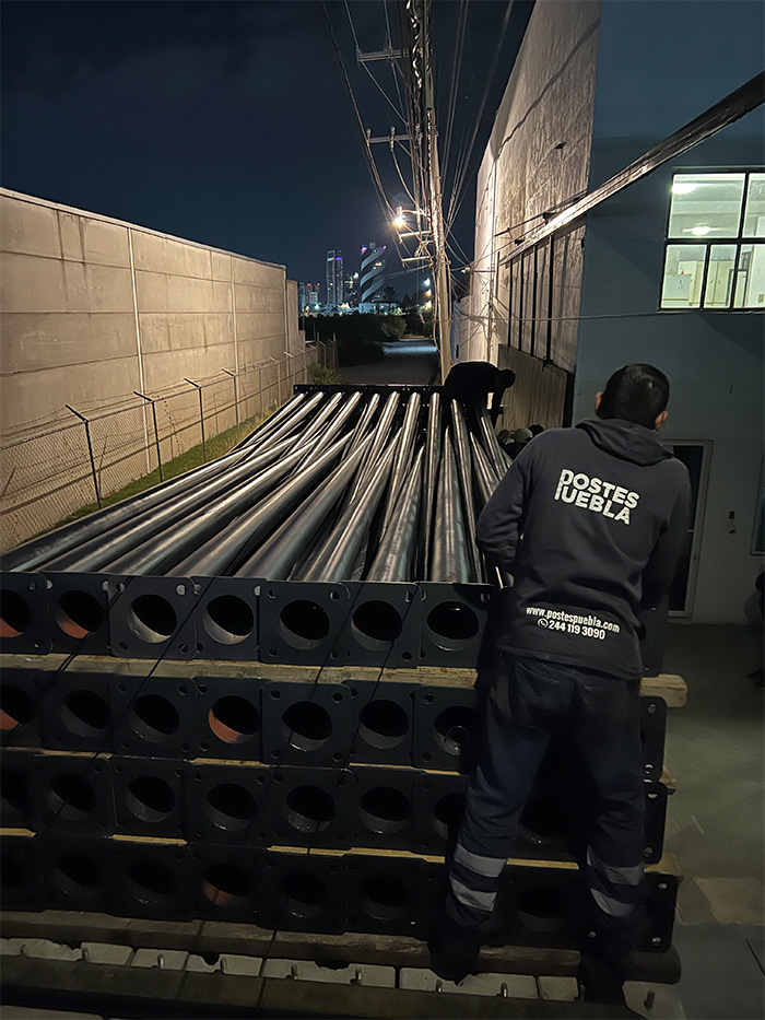 Trabajador de Postes Puebla revisando un lote de postes metálicos con placa base antes de su entrega